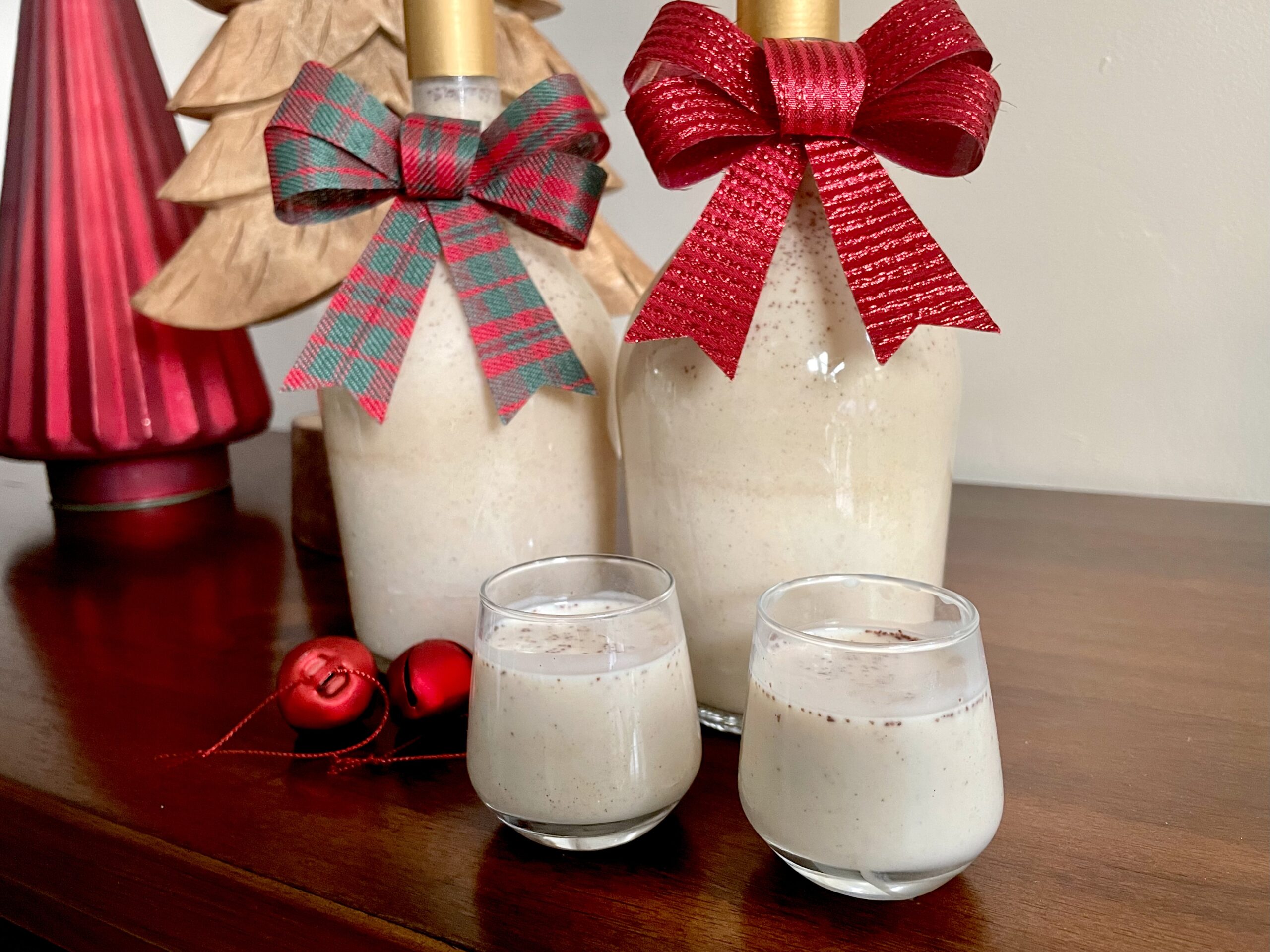 Two shot glasses filled with Cuban Coquito with bottles in the background