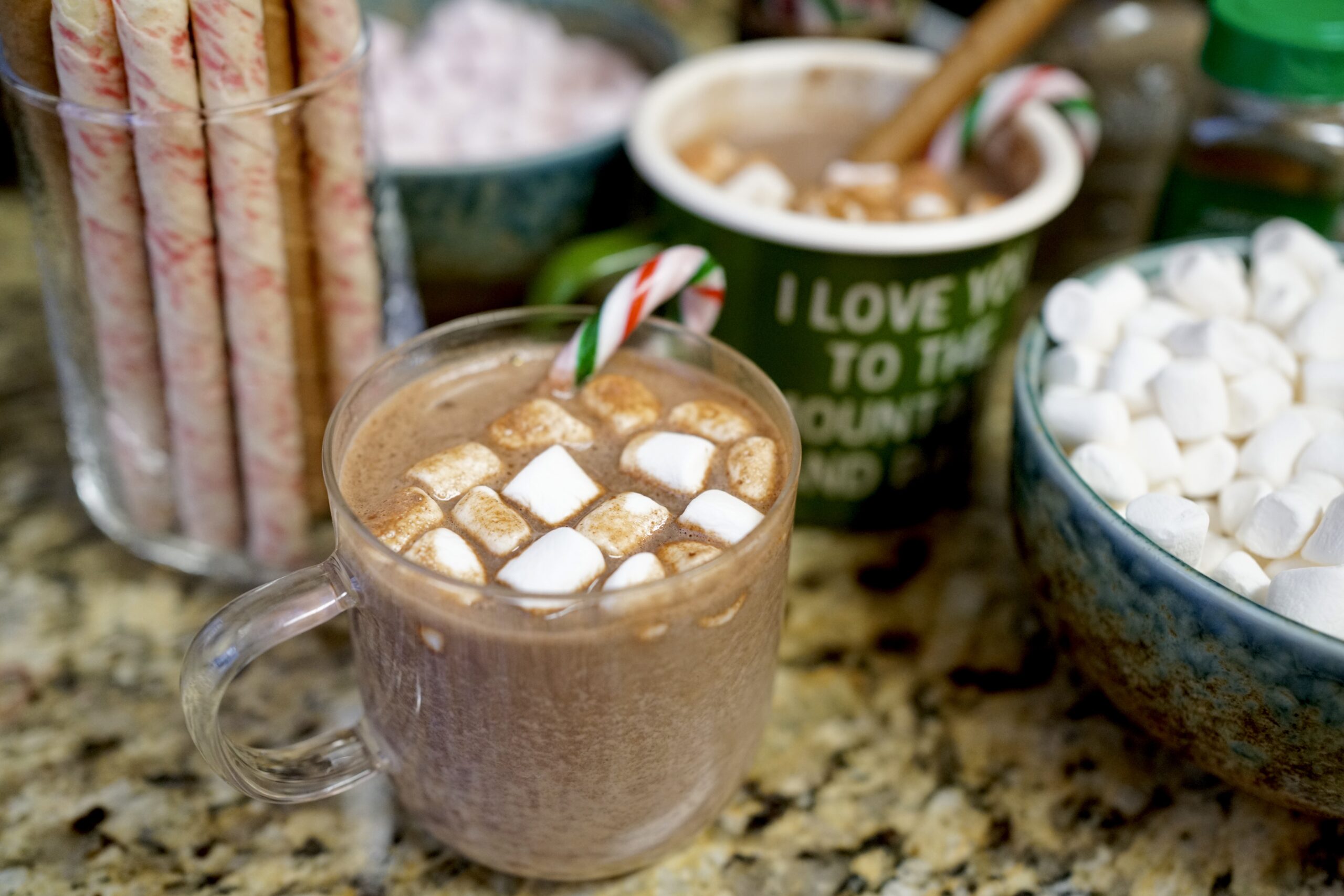 hot chocolate with candy cane surrounded by hot chocolate bar ingredients like marshmallows and cookies