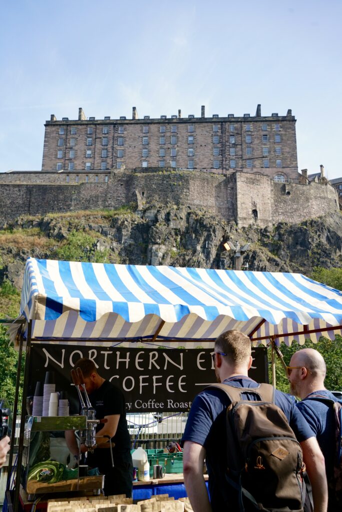 A blue and white striped farmers market stand under the Edinburgh Castle