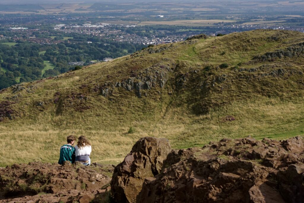 Two lovers sit and admire the view on top of Arthur's Seat