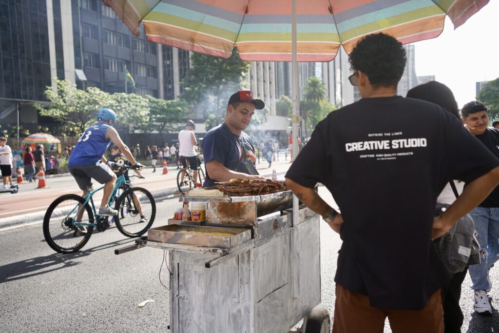 A food vendor under a colorful umbrella with a cyclists behind them