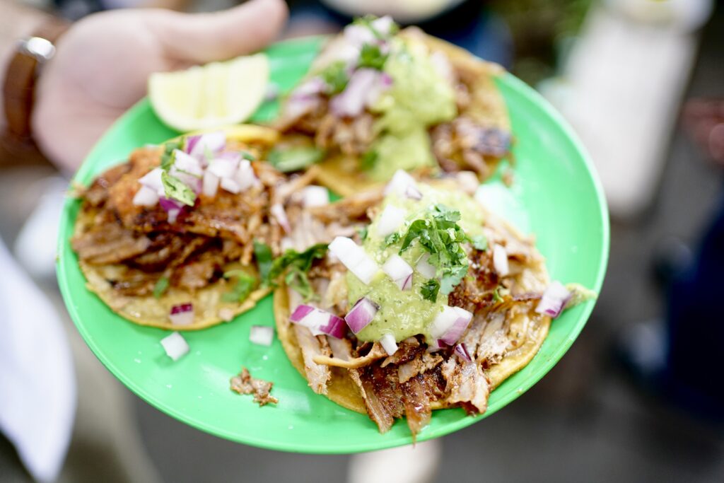 Three Mexico City-style tacos on a green plate with lime