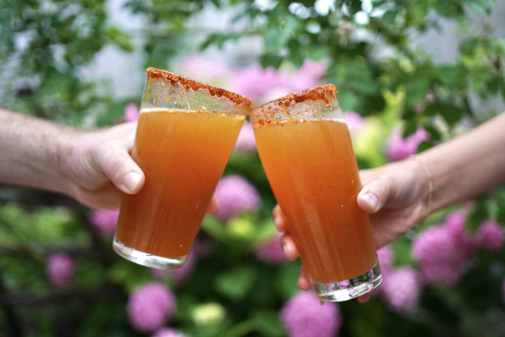 Two Michelada glasses cheers in front of a pink hydrangea bush