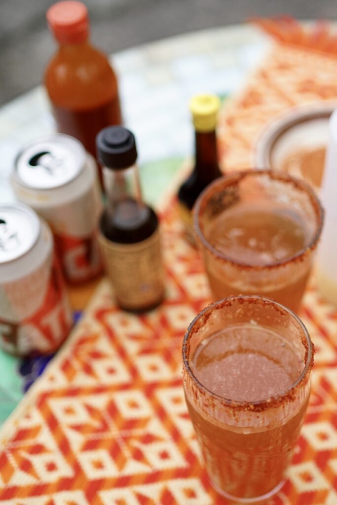 Two micheladas on a table next to seasonings