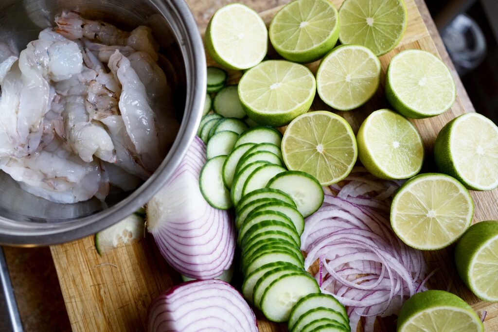 shrimp, lime, sliced cucumber, and red onion on a cutting board