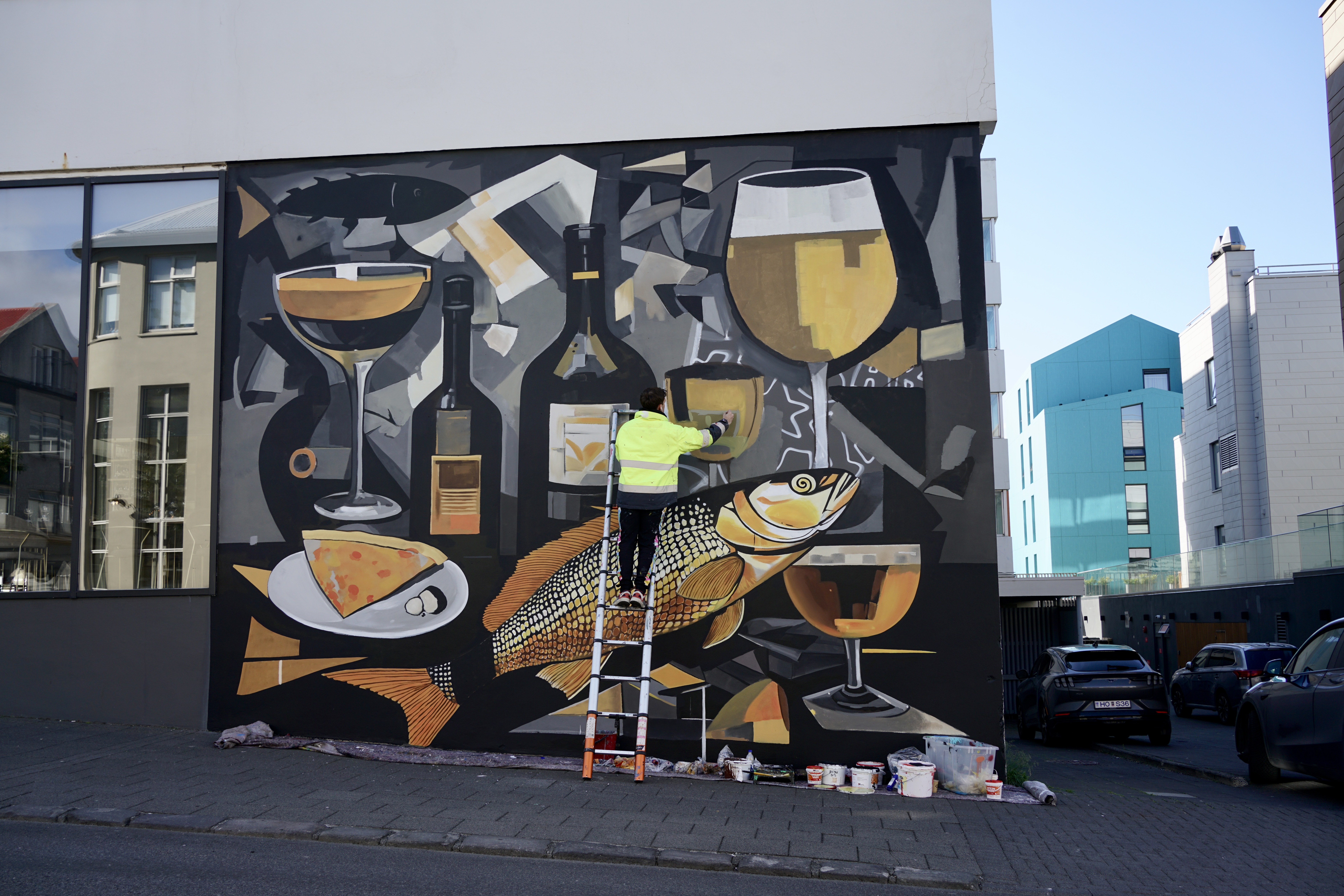 A man stands on a ladder painting a mural