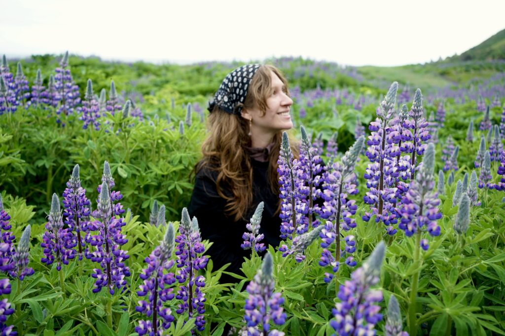 A woman smiles in a field of Lupine flowers