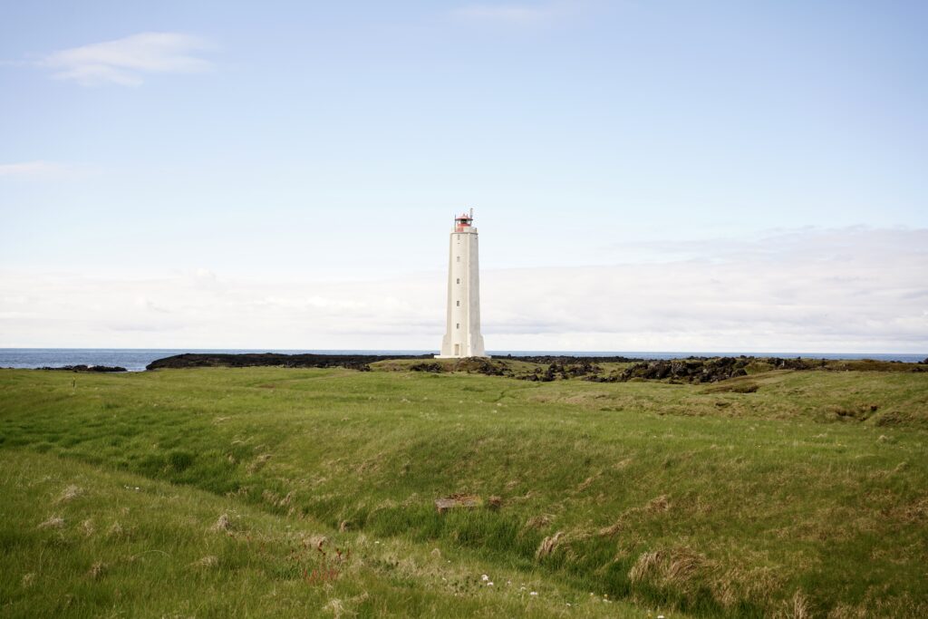 An Icelandic lighthouse at the edge of a rocky cliff with grass in the foreground