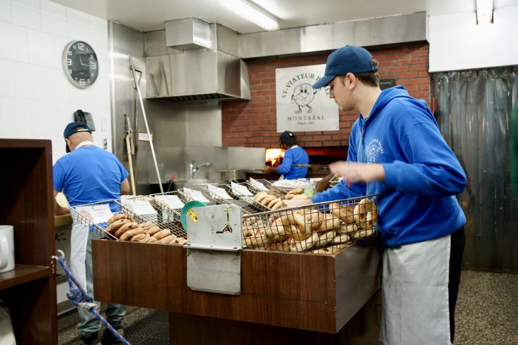 A worker throws bagel in a bin near a wood-fired oven