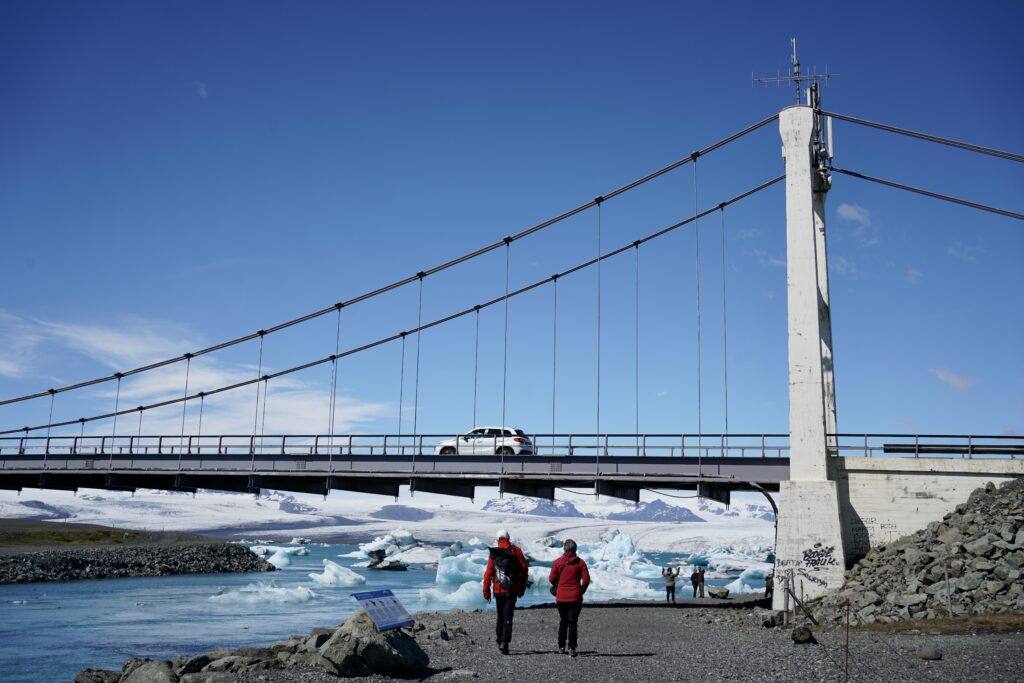two people walk under a bridge next to a glacial lagoon in Iceland