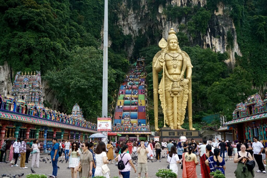 A crowd in front of the rainbow staircase and golden statue of the Batu Caves