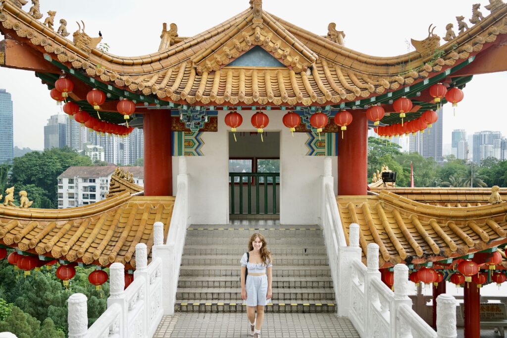 A woman stands in an outdoor corridor of a golden Chinese temple with red lanterns