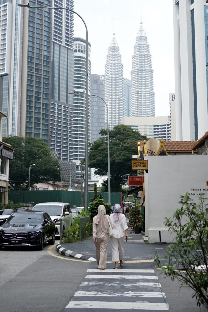 Two women walk toward the petrona towers. They look like twins walking toward the other pair of twins.