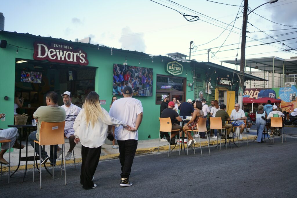 A man leads a woman past a bar on the streets of San Juan