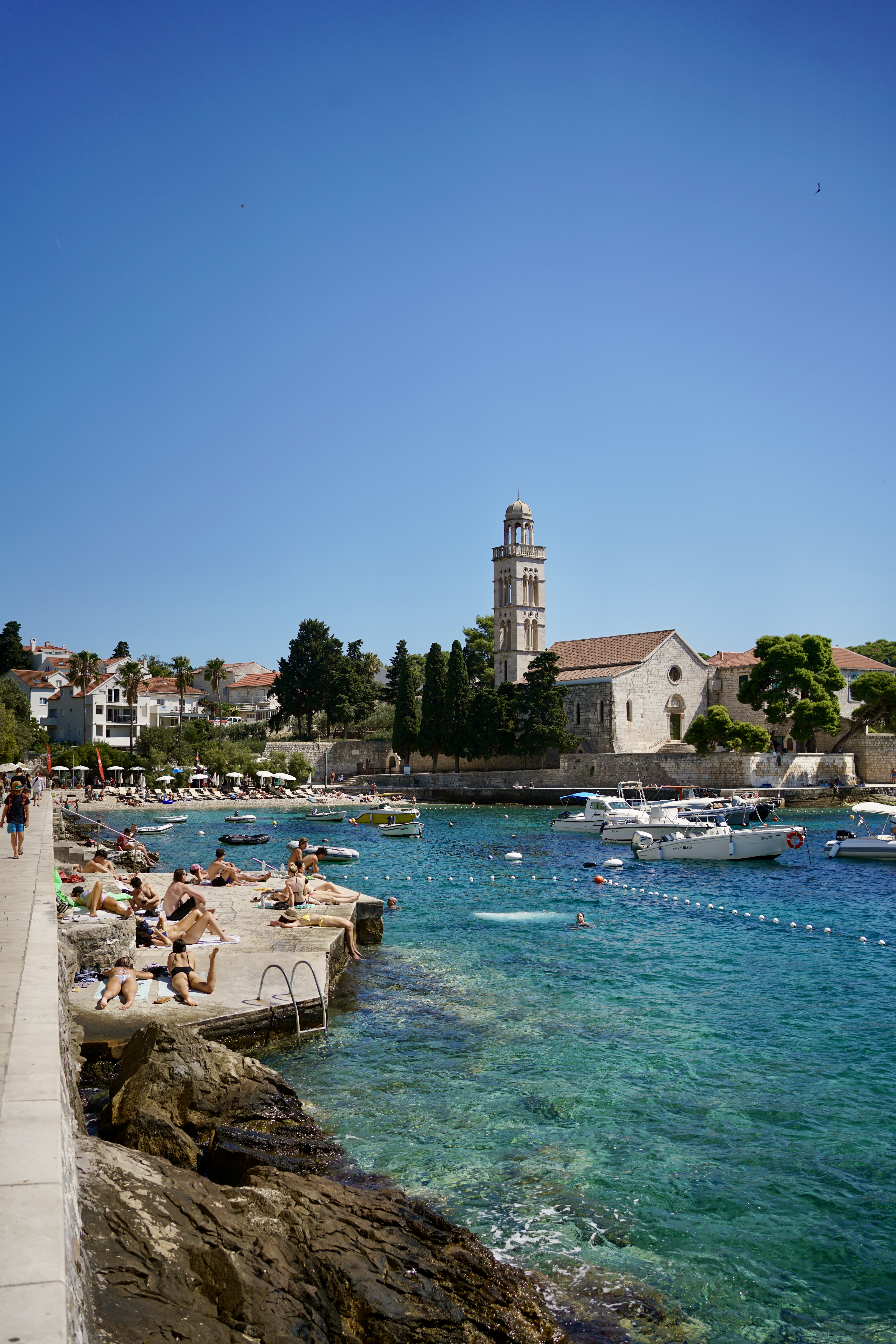 The public beach with a concrete slab going into bright blue harbor in Hvar