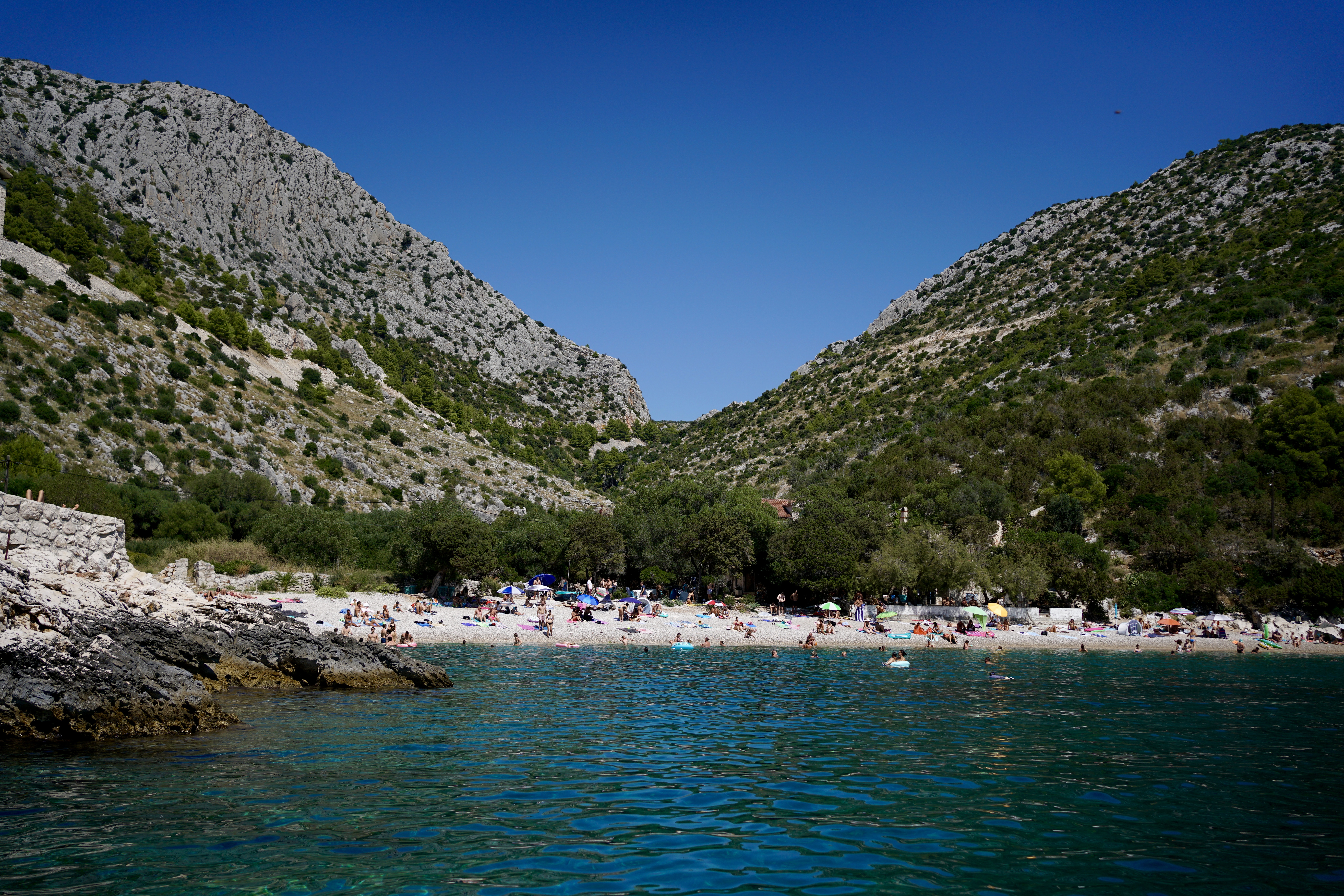 Sunbathers on a beach in the distance against mountains and blue waters