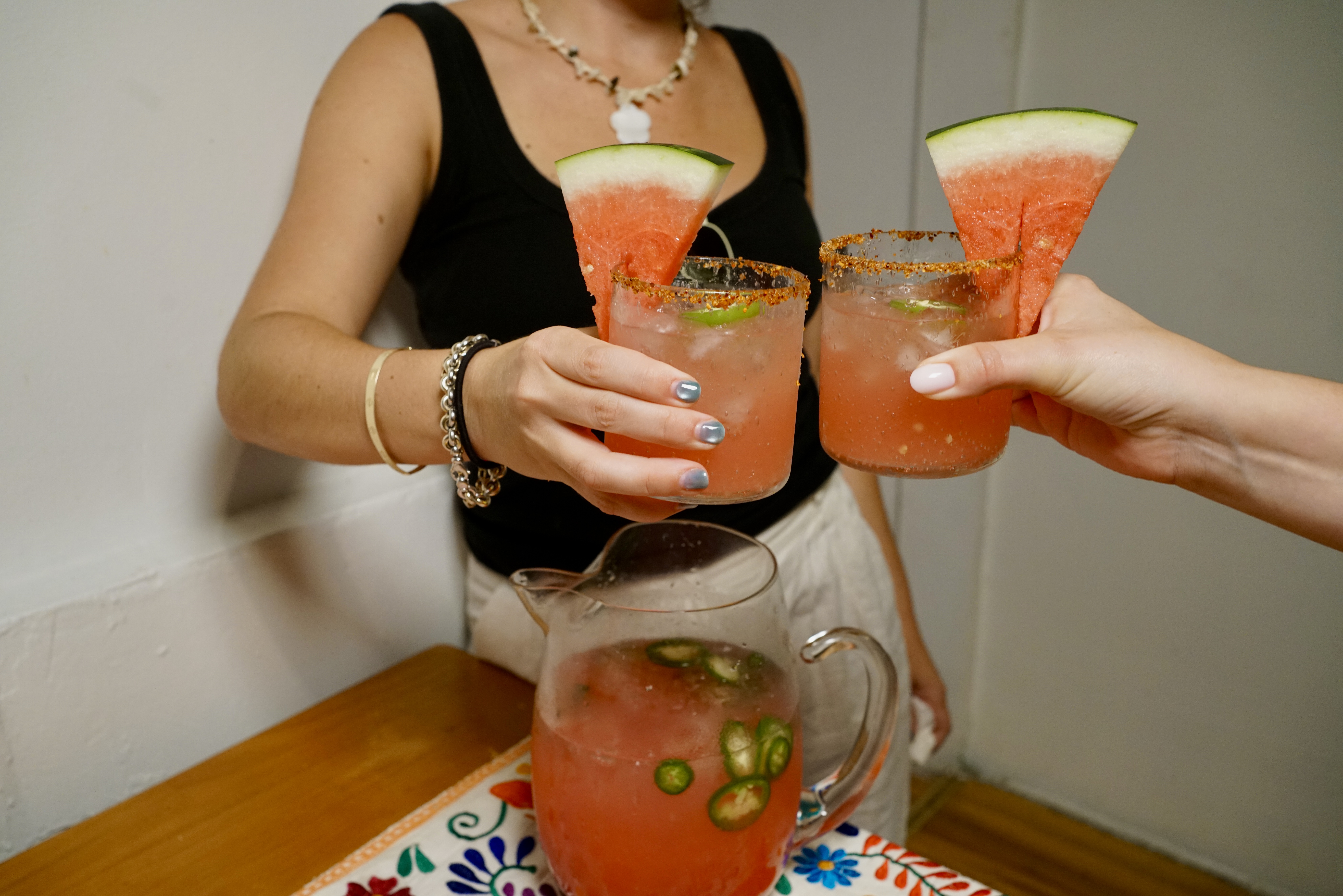 Two people cheers with a spicy watermelon margarita pitcher