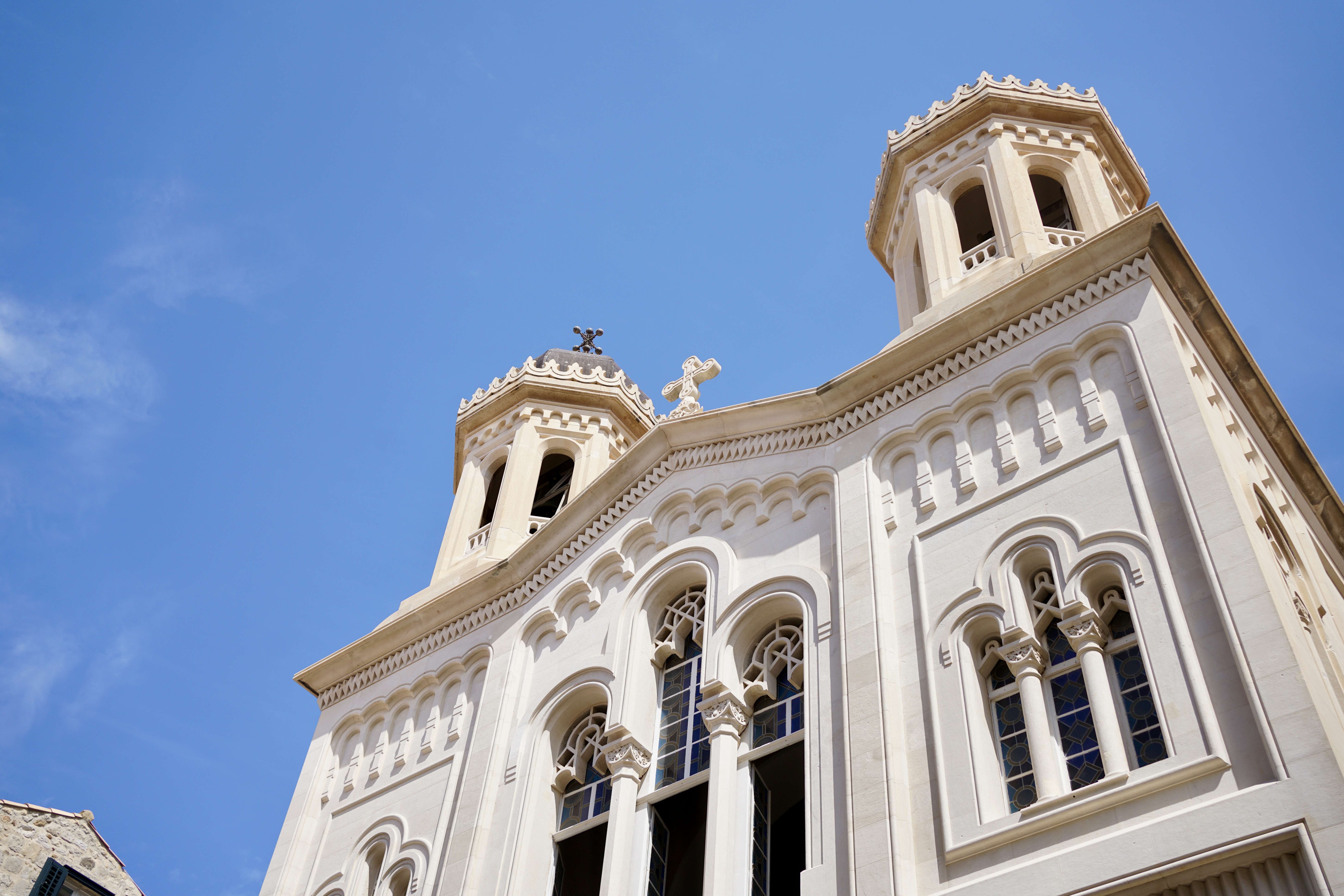 A white limestone church with two towers and a cross on top